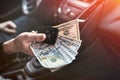 dollar and car key in male\'s hand inside car