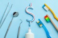 Dollar sign of toothpaste. Tube of colored toothpaste and a toothbrush and dentist tools, a mirror, a hook on a blue background. Royalty Free Stock Photo