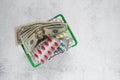 Dollars and pills in a mini grocery basket on a light background. Conceptual image of buying or selling drugs, healthcare, pharmac