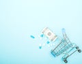 Dollars, pills and shopping cart on a blue background. Pharmacy concept. Copy space