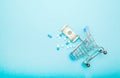 Dollars, pills and shopping cart on a blue background. Pharmacy concept. Copy space