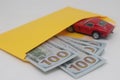 Dollars and a red car in a yellow envelope, auto purchase.