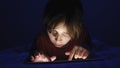 Dolly shot caucasian girl lying in bed playing tablet in internet in dark light under blacket.
