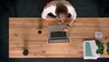 Dolly shot of top down view of casually-dressed woman working and making notes in office in front of the laptop.