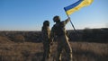 Dolly shot of young woman and man in military uniform waving flag of Ukraine against sunset. Female and male soldier of Royalty Free Stock Photo