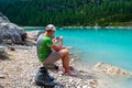 Barefoot hiker standing on a rock with his boots next to him and taking a picture with his phone at Lago di Sorapis