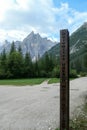 Dolomites UNESCO World Heritage sign next to a gravelled road leading along a lush green meadow to Italian Dolomites.