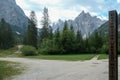 Dolomites UNESCO World Heritage sign next to a gravelled road leading along a lush green meadow to Italian Dolomites.