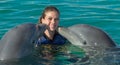 Dolphins kiss young woman in blue water. Smiling woman swimming with dolphin. Blue ocean water background