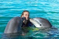 Dolphins kiss young woman in blue water. Smiling woman swimming with dolphin. Blue ocean water background