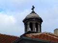The dome of an old chapel with a cross over the tiled roofs against the sky
