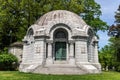 Dome-shaped stone mausoleum with Christian symbols and wrought-iron gate with trees in the background