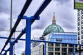 Dome and spire of the historic Berlin Cathedral behind a modern glass facade of a hotel and blue overhead lines in the foreground