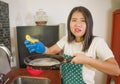 Domestic chores lifestyle portrait of young tired and stressed Asian Chinese woman in cook apron washing dishes at kitchen sink Royalty Free Stock Photo