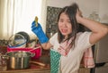 Domestic chores lifestyle portrait of young tired and stressed Asian Korean woman in cook apron washing dishes at kitchen sink Royalty Free Stock Photo