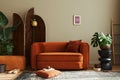 Domestic interior of living room with design sofa, mock up poster frames, plants, pouf, room screen, elegant side table.