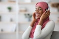 Domestic Leisure. Relaxed Black Muslim Lady In Hijab Listening Music In Headphones