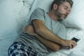 Domestic lifestyle high angle portrait of young attractive and tired man sleeping on bed holding mobile phone in internet and Royalty Free Stock Photo