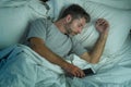 Domestic lifestyle high angle portrait of young attractive and tired man sleeping on bed holding mobile phone in internet and Royalty Free Stock Photo