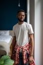Domestic portrait of bearded African American guy in casual clothes standing in modern apartment