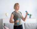 Domestic training concept. Strong mature woman exercising with dumbbells at home