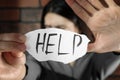 Domestic violence concept. Unhappy woman holding paper with written word Help near brick wall, focus on hands Royalty Free Stock Photo