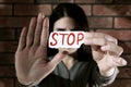 Domestic violence concept. Woman holding paper with word Stop near brick wall, focus on hands Royalty Free Stock Photo