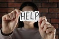 Domestic violence concept. Woman holding paper with written word Help near brick wall, focus on hands Royalty Free Stock Photo