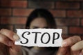 Domestic violence concept. Woman holding paper with written word Stop near brick wall, focus on hands Royalty Free Stock Photo