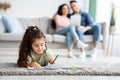 Domestic Weekend. Small Girl Drawing With Pencils While Parents Relaxing On Couch Royalty Free Stock Photo