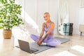 Domestic yoga concept. Young fit lady doing butterfly stretch exercise, meditating at home in front of laptop