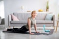 Domestic yoga practice. Flexible mature woman doing cobra pose on mat, following online sports video at home, copy space
