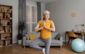 Domestic yoga practice. Senior woman standing in tree pose, keeping balanced, training at home in living room