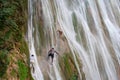 Young guys climb the ledges of a cliff on the waterfall