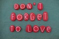 Don`t forget to love, creative phrase composed with red colored stone letters over green sand