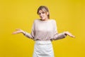 Don`t know! Portrait of uncertain young woman with blonde hair in casual beige blouse, isolated on yellow background