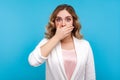 Don`t tell! Portrait of frightened woman covering mouth with hand scared to speak. isolated, blue background
