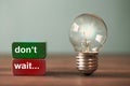 Don`t wait are the word written on a red and a green toy block. Next to the tow blocks, an ancient light bulb with glowing light Royalty Free Stock Photo