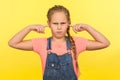 Don`t want to listen. Portrait of capricious little girl in denim overalls standing with closed ears not to hear parental advice
