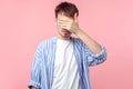 Don`t want to watch! Portrait of young serious brown-haired man with small beard covering eyes with hand. isolated on pink Royalty Free Stock Photo