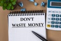 DON`T WASTE MONEY - words in a white notebook on the background of a calculator, sheets of paper and a cactus