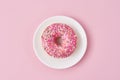 Donat decorated sprinkles and icing in white plate on a pink background. Creative and minimalis food concept, top view flat lay