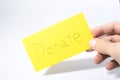 Donate handwrite witha a hand on a yellow paper