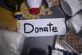 `Donate` sign handwritten with black letters. A pile of food supplies on a grey table. Food donation concept. Context of
