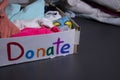 `Donate` sign handwritten with multicoloured letters. A box with clothes and a pile of clothes nearby on a grey table