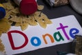 `Donate` sign handwritten with multicoloured letters. A pile of food supplies on a grey table. Food donation concept