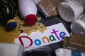 `Donate` sign handwritten with multicoloured letters. A pile of food supplies on a grey table. Food donation concept