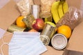 Donation box with various food and protective medical mask. Cardboard box with cereals, canned goods and fruits Royalty Free Stock Photo