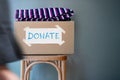 Donation Concept. Donate Box with Used Old Clothes on Chair against Wall in Public Space. blurred walking people as forground