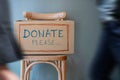 Donation Concept. Empty Donate Box on Chair against Wall in Public Space. blurred walking people as forground